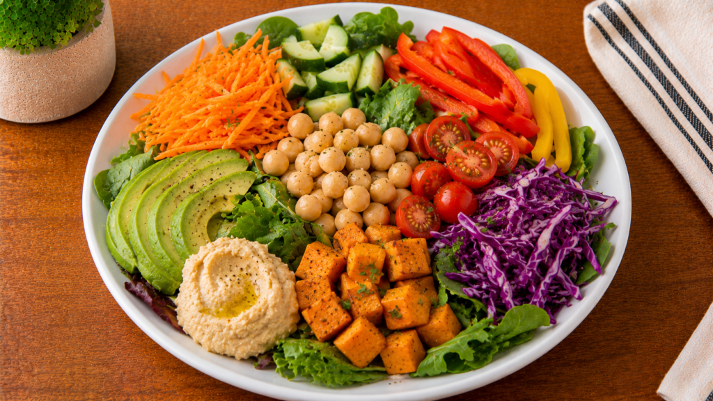 Colorful plate filled with a variety of vegetables including carrots, bell peppers, greens, tomatoes, and other fresh produce on a wooden countertop.
