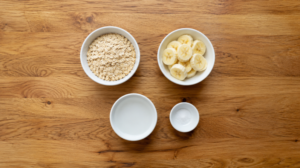 Small white bowls with oats, sliced banana, and liquid arranged neatly on a wooden surface.