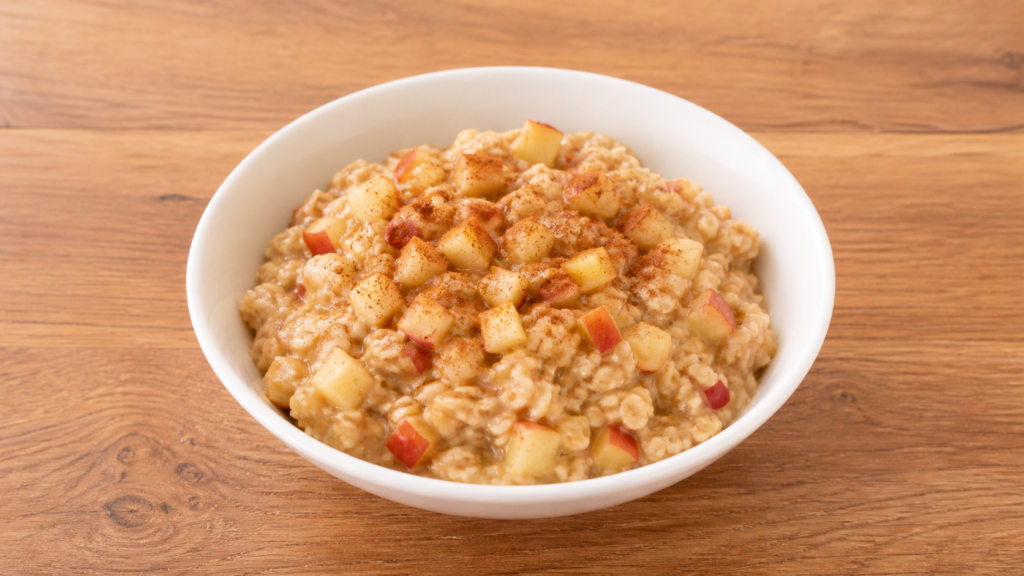 A white bowl of warm apple cinnamon oats with diced apples on a wooden countertop in soft natural light.
